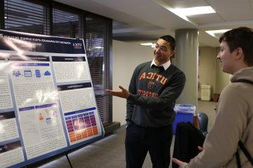 A student makes a presentation by a poster at the 2024 Student Conference for Research, Professional Activities, and Creative Arts.